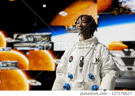 Cheerful astronaut in high tech spacecraft monitoring mission data on displays. Jolly spacecraft cosmonaut prepares for space travel operations, looking at multimedia digital backdrop 137176627