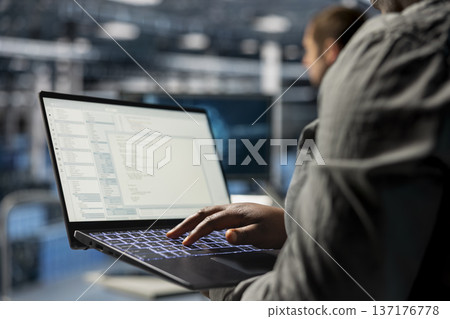 Close up of data center programmer looking at code debugging tools running on laptop. Server farm IT professional typing on notebook keyboard, writing script automating tasks Close up of data center programmer looking at code debugging tools running on laptop. Server farm IT professional typing on notebook keyboard, writing script automating tasks 137176778