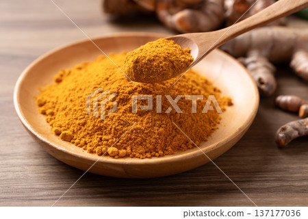 Turmeric powder in a wooden bowl with a wooden spoon scooping it 137177036