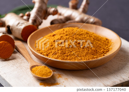 Turmeric powder in a wooden bowl with a wooden spoon and fresh turmeric roots  137177040