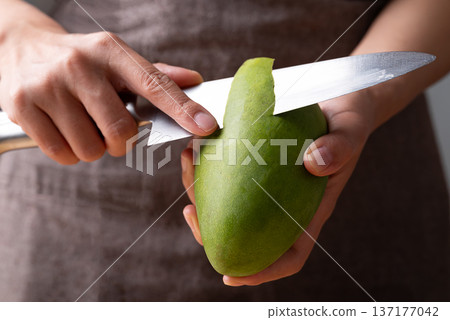 Close up of hand holding knife and peeling green mango Close up of hand holding knife and peeling green mango 137177042