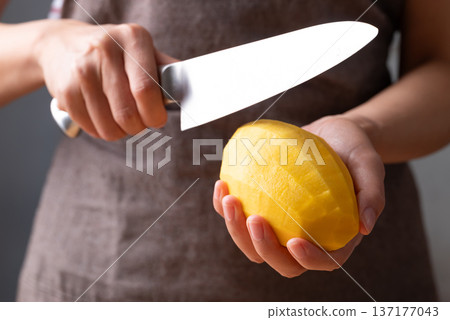 Close up of hand holding peeled mango and slicing with a knife 137177043