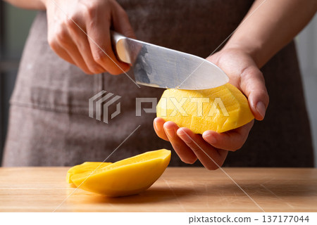 Close up of hand holding a knife slicing mango 137177044