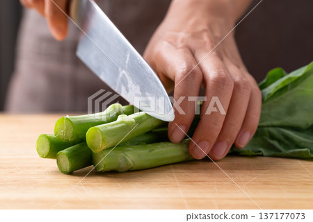 Hand using a knife to cut fresh Chinese kale or Chinese broccoli (Gai Lan) on wooden board Hand using a knife to cut fresh Chinese kale or Chinese broccoli (Gai Lan) on wooden board 137177073