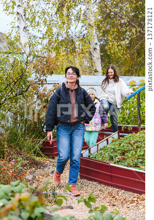Smiling Russian women and a child walking together in a village garden on an autumn day. Warm friendship, happiness, and meeting with friends. Smiling Russian women and a child walking together in a village garden on an autumn day. Warm friendship, happiness, and meeting with friends. 137178121