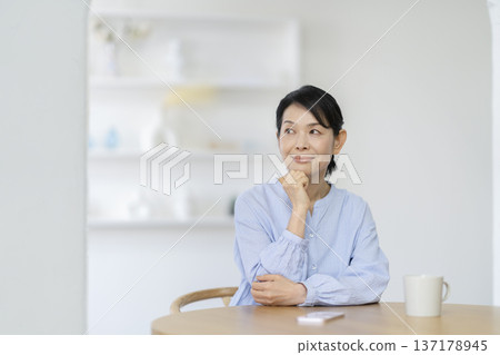 A woman in her late 50s sitting at a dining table and smiling 137178945