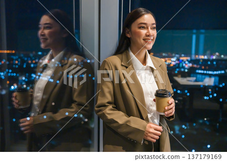 Businesswoman holding coffee cup in office with city lights background at night 137179169