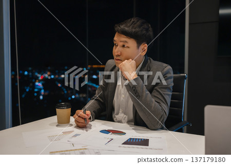 worried businessman thinking and analyzing business reports late at night in office with city lights background worried businessman thinking and analyzing business reports late at night in office with city lights background 137179180