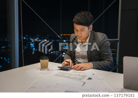 businessman analyzing financial reports and using calculator to data analysis in business office with city lights background at night 137179181