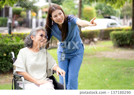 Caucasian female caregiver encouraging senior patient on wheelchair in garden. Caucasian female caregiver encouraging senior patient on wheelchair in garden. 137180290