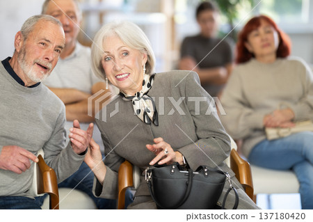 Communicative older man and woman talking while sitting among focused group of people listening lecture in conference hall Communicative older man and woman talking while sitting among focused group of people listening lecture in conference hall 137180420