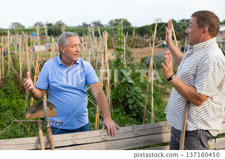 Two male gardeners talking near wooden fence in garden Two male gardeners talking near wooden fence in garden 137180450