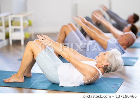 Elderly woman during group workout performs exercises to strengthen muscles of press Elderly woman during group workout performs exercises to strengthen muscles of press 137180466