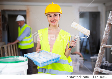 Cheerful woman builder holding paint roller and tray, home improvement works Cheerful woman builder holding paint roller and tray, home improvement works 137180620