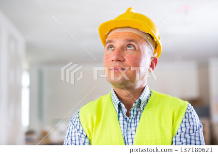 Portrait of smiling worker in yellow vest and hard hat inside cottage under renovation Portrait of smiling worker in yellow vest and hard hat inside cottage under renovation 137180621