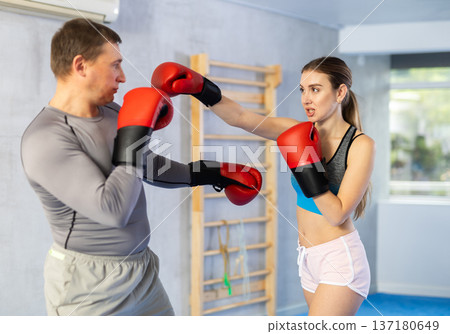Young girl training boxing with middle-aged male trainer during sports classes Young girl training boxing with middle-aged male trainer during sports classes 137180649