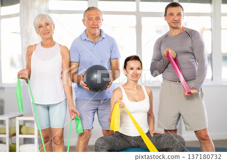 Group of women and men of different ages in sportswear with fitness balls and resistance bands posing together in sports studio, ready for training 137180732