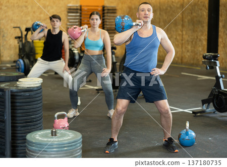 Active middle-aged man in sportswear exercising CrossFit with kettlebell while training with group in fitness center 137180735