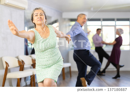 Smiling adult lady in elegant clothes learn to dance couples latin dance, energetic and fast jive in dance salon Smiling adult lady in elegant clothes learn to dance couples latin dance, energetic and fast jive in dance salon 137180887