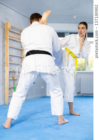 Young girl and middle-aged man practicing foot kicks and blocks in pair during karate courses 137180902
