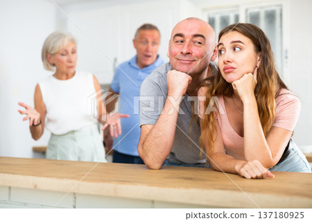 Husband and wife listen to their parents scold them in home kitchen 137180925
