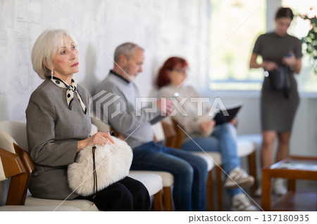 Elderly man and woman in casual clothes waiting for turn on chair in reception Elderly man and woman in casual clothes waiting for turn on chair in reception 137180935