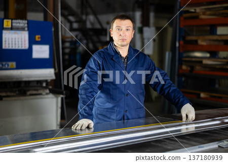 Experienced worker measuring metal sheet with tape measure in workshop 137180939