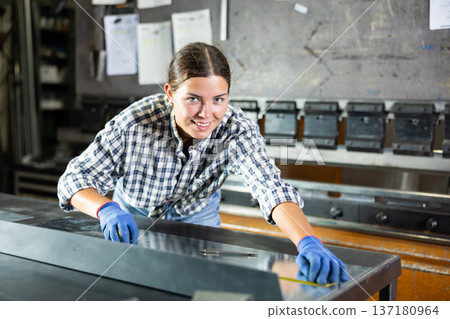 Smiling female worker marking steel sheet with tape measure in workshop Smiling female worker marking steel sheet with tape measure in workshop 137180964