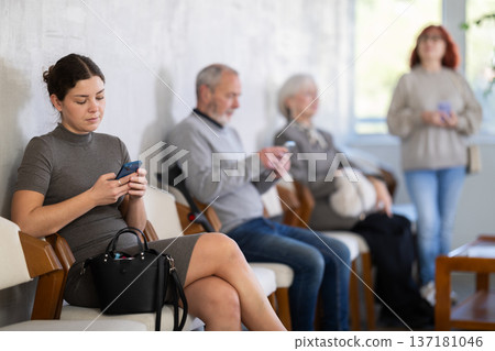 Young girl sitting in clinic waiting area scrolling mobile phone Young girl sitting in clinic waiting area scrolling mobile phone 137181046