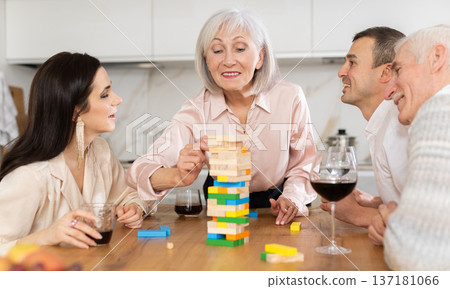 Joyful senior parents and young couple sitting around table playing brick game Joyful senior parents and young couple sitting around table playing brick game 137181066