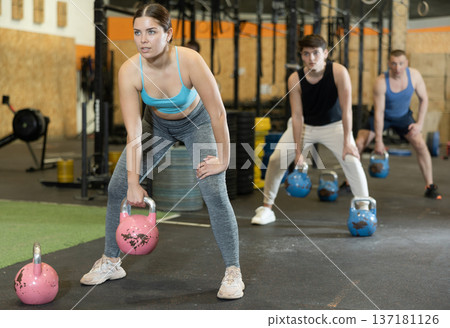 Sporty young girl doing exercises with kettlebell at workout 137181126