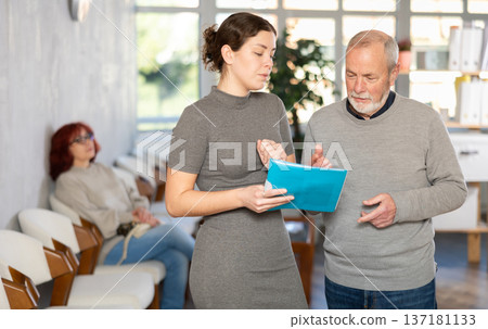 Young secretary talking with elderly man in reception area 137181133