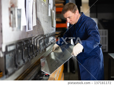 Metallurgical plant - male worker bending sheet of metal on press Metallurgical plant - male worker bending sheet of metal on press 137181172