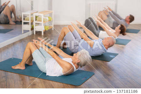 Group of elderly women and men practicing pilates exercises in gym. Abdominal press training Group of elderly women and men practicing pilates exercises in gym. Abdominal press training 137181186