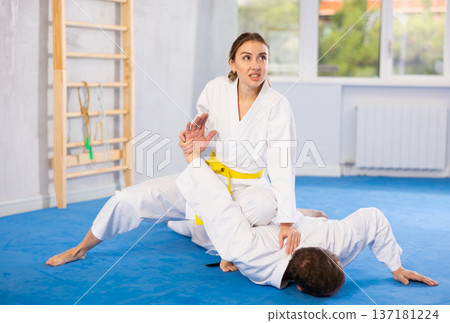 Coach teaches young woman techniques for wrestling and throwing on sports mats during judo training Coach teaches young woman techniques for wrestling and throwing on sports mats during judo training 137181224