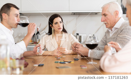 Joyful senior parents and young couple sitting around table playing poker Joyful senior parents and young couple sitting around table playing poker 137181263
