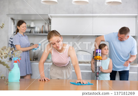 Teenage girl wiping table while cleaning house with family 137181269