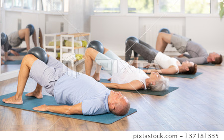Elderly man performs glute bridge with softball in knees Elderly man performs glute bridge with softball in knees 137181335
