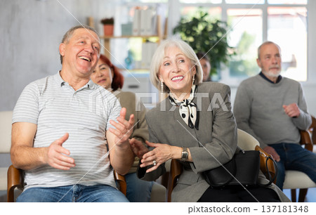 Joyful and happy group of people of different ages sitting on chairs, listening lecture and laughing in conference hall Joyful and happy group of people of different ages sitting on chairs, listening lecture and laughing in conference hall 137181348
