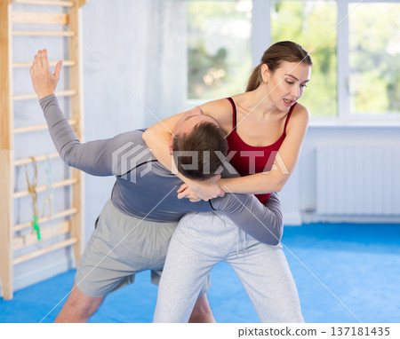 Young woman learning to do power grab on an opponent neck during self-defense training at gym Young woman learning to do power grab on an opponent neck during self-defense training at gym 137181435