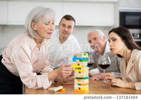Group of mature spouses and son with girlfriend is playing board game with wooden blocks in kitchen 137181484