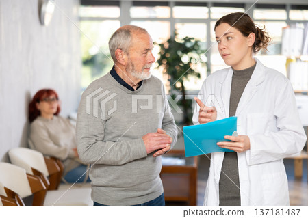 Nurse or doctor talk with mature man in reception area Nurse or doctor talk with mature man in reception area 137181487
