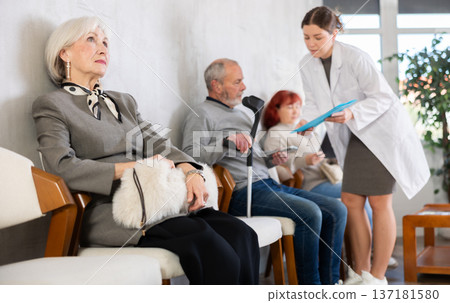 Elderly people wait in line at clinic. Nurse talks to patient in background 137181580