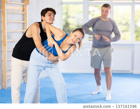 Self-defense class - a woman learns to fight back an attacking man under the guidance of trainer 137181596