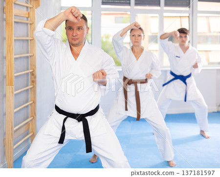 Woman and man in kimono standing in fight stance during group karate training in gym 137181597