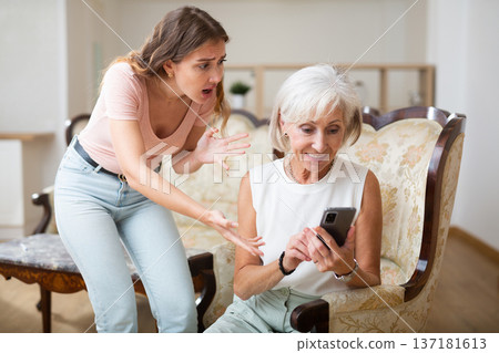 Young woman outraged when looking into phone of old mother Young woman outraged when looking into phone of old mother 137181613