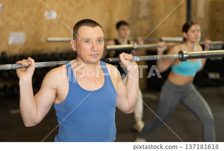Dedicated man doing sit-ups with rod among other people in gym Dedicated man doing sit-ups with rod among other people in gym 137181618