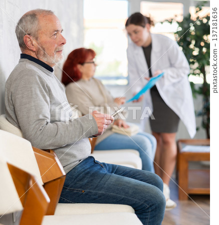 Elderly man sitting in clinic queue while nurse talks to other patients 137181636