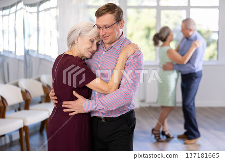 Happy senior woman and man dancing slow ballroom dance during group class in studio Happy senior woman and man dancing slow ballroom dance during group class in studio 137181665