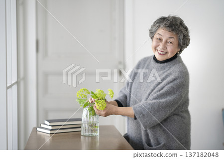 一位老婦人用鮮花裝飾房間,她看著鏡頭,面帶微笑。 一位老婦人用鮮花裝飾房間,她看著鏡頭,面帶微笑。 137182048